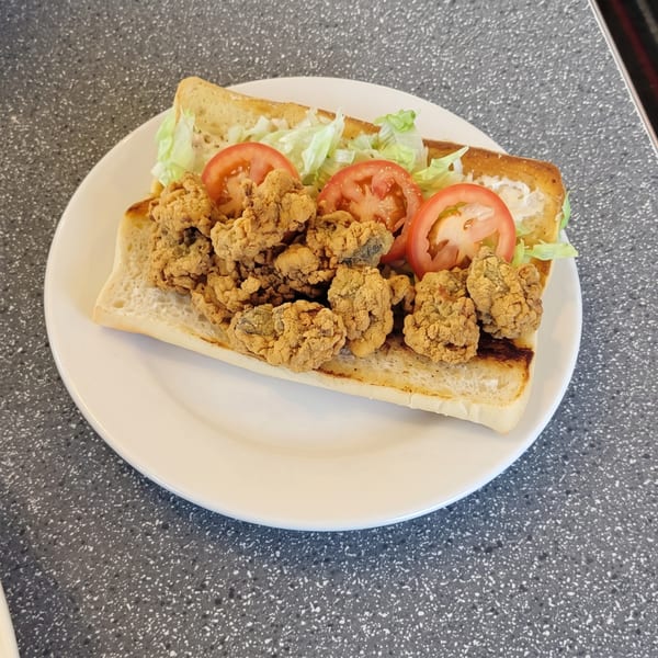 Fried oyster po'boy sandwich with lettuce and tomato on a white plate.
