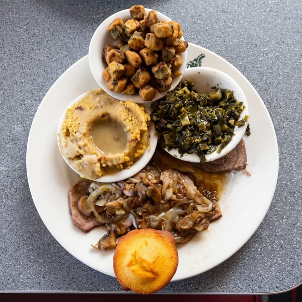 A plate of country-fried steak with gravy, mashed potatoes, collard greens, fried okra, and cornbread.