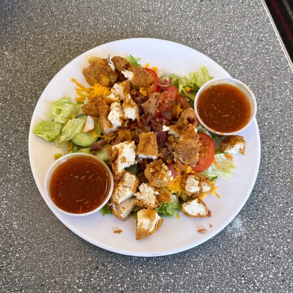 Crispy fried chicken salad with lettuce, tomatoes, cheese, bacon bits, and two cups of dressing.
