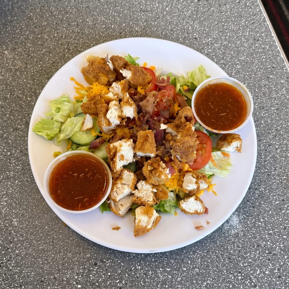 Crispy fried chicken salad with lettuce, tomatoes, cheese, bacon bits, and two cups of dressing.